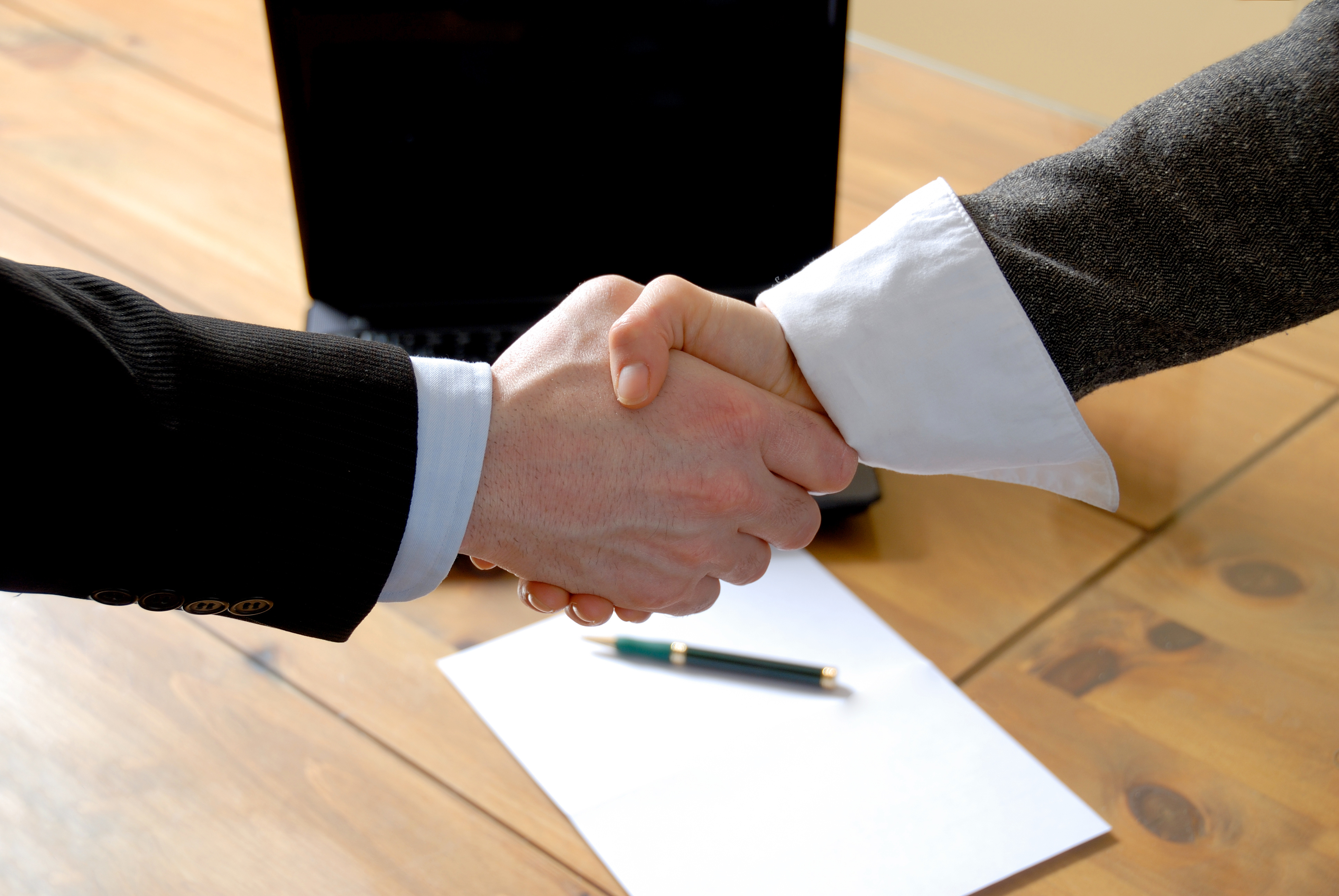 man and woman shaking hands in front of laptop